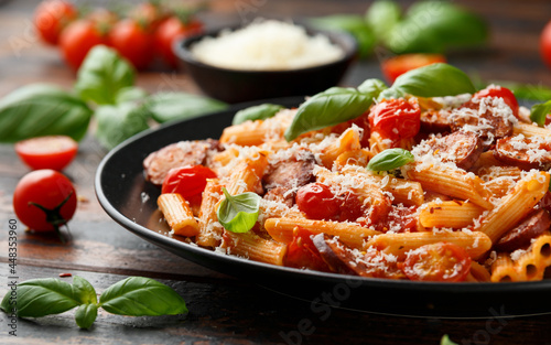 Sausage penne Pasta with tomato sauce, parmesan cheese and basil on black plate