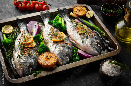 Raw Dorado fish with vegetables in a metal tray. Fish cooking recipe. Top view. Free copy space. On a black stone background.