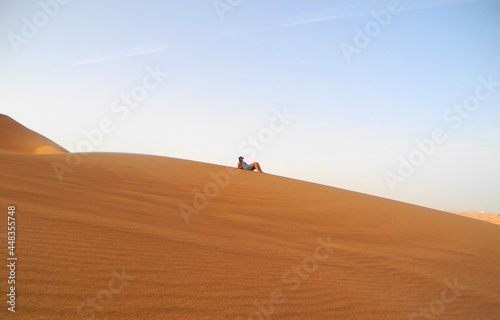 Girl laying down on a huge sand dune in the far distance and contemplating over life in a relaxed state.