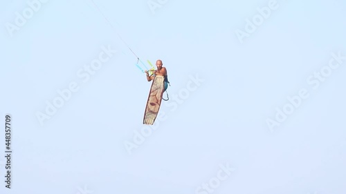 Young adult caucasian fit male person enjoy riding kite surf board macking extreme trick stunt bright sunny day against blue sky at sea or ocean shore. Watersport adrenaline fun adventure acitivity