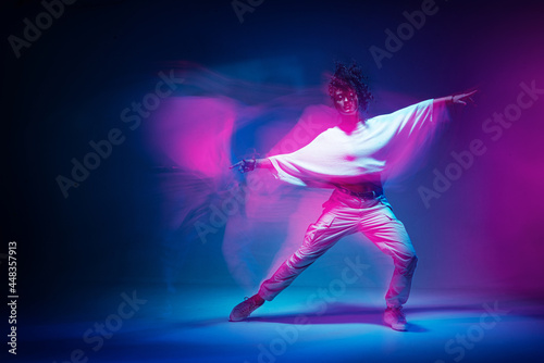 Mixed race female dancing in colorful neon light. Studio photo with long exposure. Expressive contemporary hip hop dance