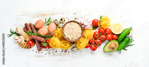 White wooden food background: tomatoes, pasta, spices, vegetables and sausages. Top view.