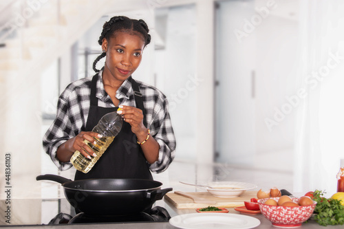 Afro american woman holding an oil bottle behind a deep frying pan