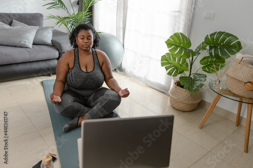 Young African curvy woman doing yoga virtual fitness class with laptop at home - Sport wellness people lifestyle concept