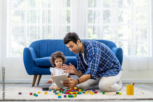 Modern Remote Communication Concept. Portrait of positive caucasian father making virtual video call with mother using tablet, while the little daughter was playing with colorful wooden blocks