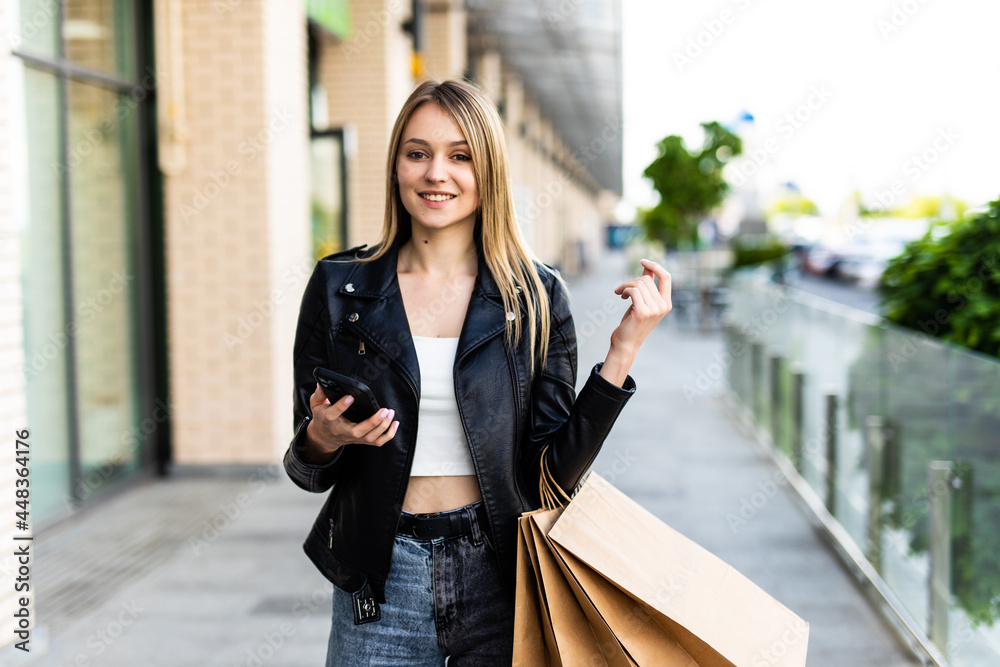 Front view portrait of a happy shopper shopping and using a smart phone in a mall