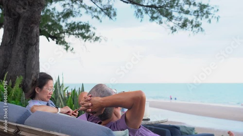 senior asian couple sitting on bench near beach during summer vacation
