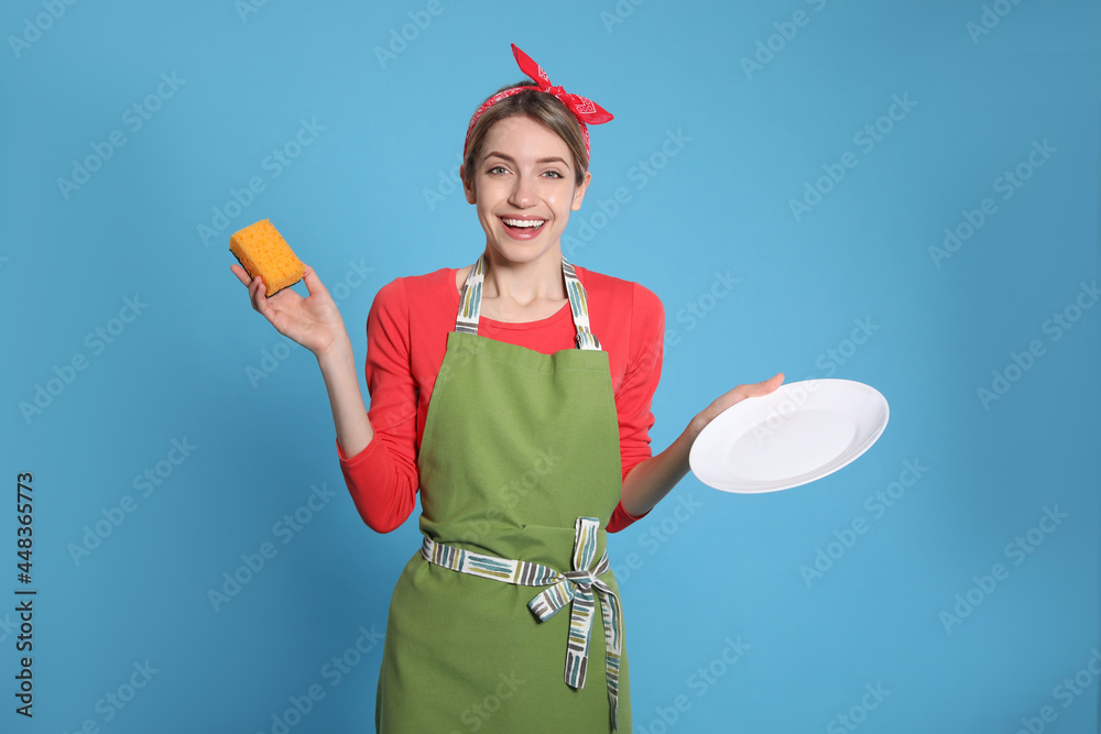 Young housewife with plate and sponge on light blue background Young housewife with plate and sponge on light blue background