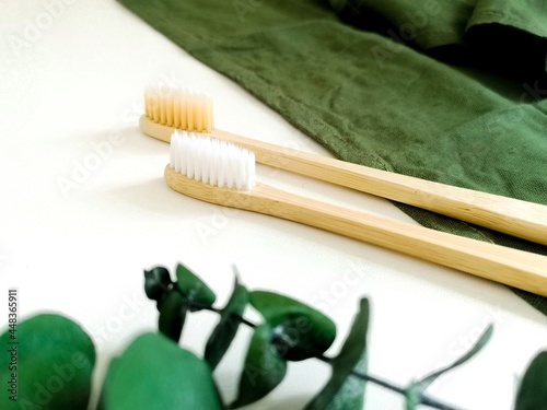 Two bamboo toothbrushes on a green towel with a plant on the background