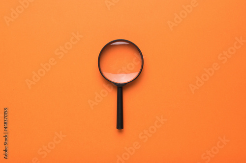 Magnifying glass with a handle on an orange background. Flat lay.