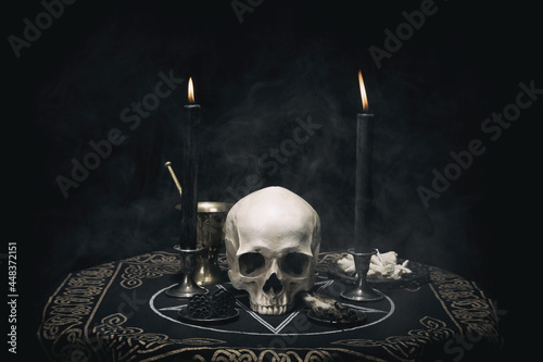 Witchcraft composition with burning candles, human skull, bones, herbs and pentagram symbol. Halloween and occult concept, black magic ritual. 