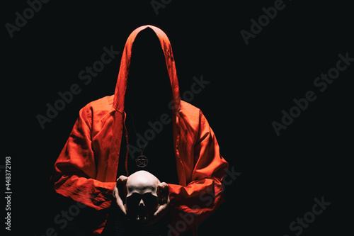 Man in red ritual hooded cloak holds a human skull in hands. Religious sects, satanism, occult, esoteric, concept. Copy space. photo