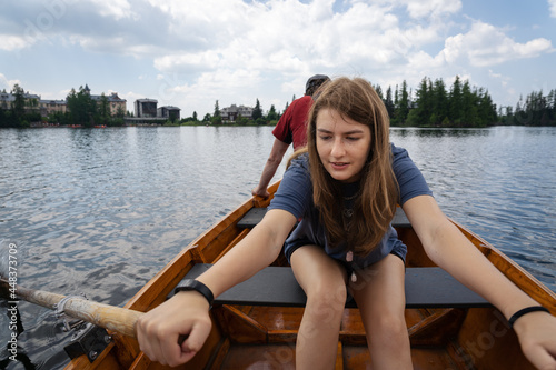 Teenage girl rowing boat on Strbske pleso (Strba tarn) in High Tatra mountains, Slovakia. Scenic landscape in background. Summer holiday concept