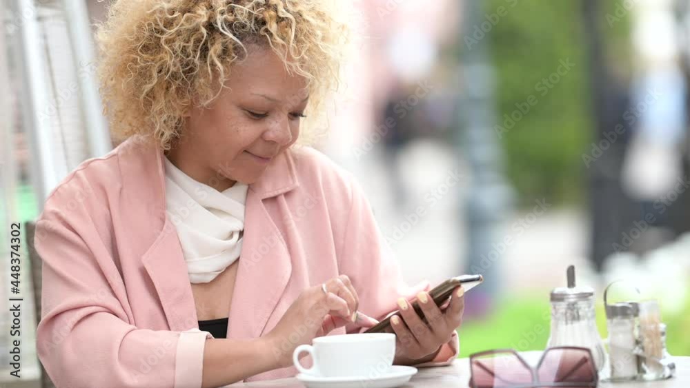 Happy African American businesswoman sitting at the street cafe Using Smartphone. Communication, online shopping, social network concept. Happy African American businesswoman sitting at the street cafe Using Smartphone. Communication, online shopping, social network concept.