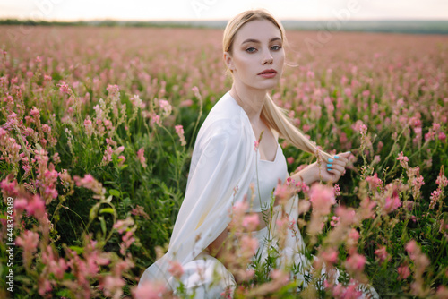 Beauty romantic girl Outdoors at sunset. Young woman in stylish clothes posing in the blooming field. Nature, vacation, relax and lifestyle. Fashion concept.