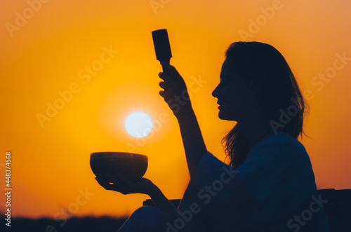 Cinematic silhouette of woman playing a Tibetan bowl at gorgeous orange sunset with sun disk. Concept: peace, tranquility, zen, spirituality, sound healing photo