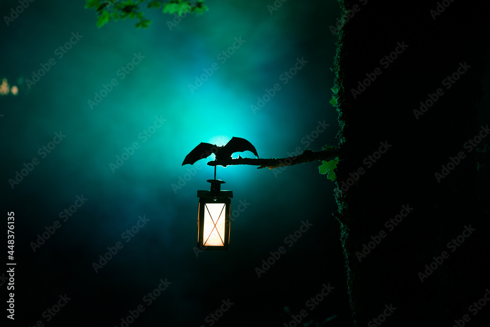 Horror Halloween concept. The bat is spreading its wings sitting on the tree at misty night.