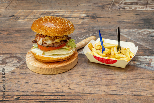 Classic beef burger with bread with sesame seeds, tomato and lettuce and fried ham loaches with fried onion with French fries as garnish