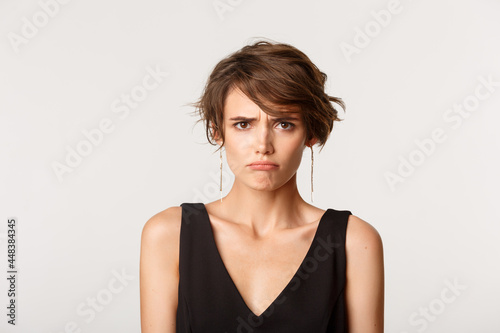 Close-up of timid angry cute girl, sulking and looking offended, standing over white background