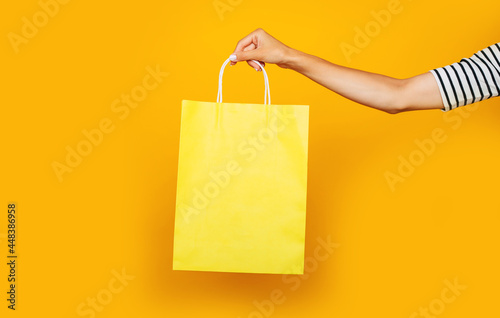Close up photo of female hand with colorful shopping bag in hands isolated on yellow background