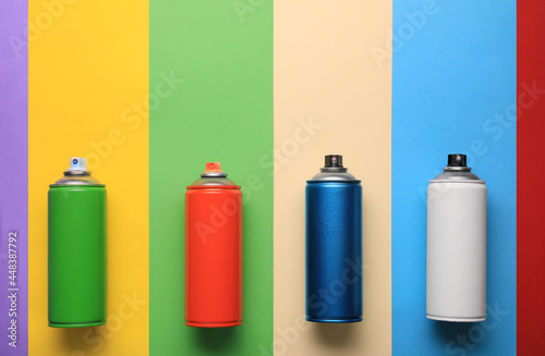 Cans of different spray paints on color background, flat lay with space for text. Graffiti supplies