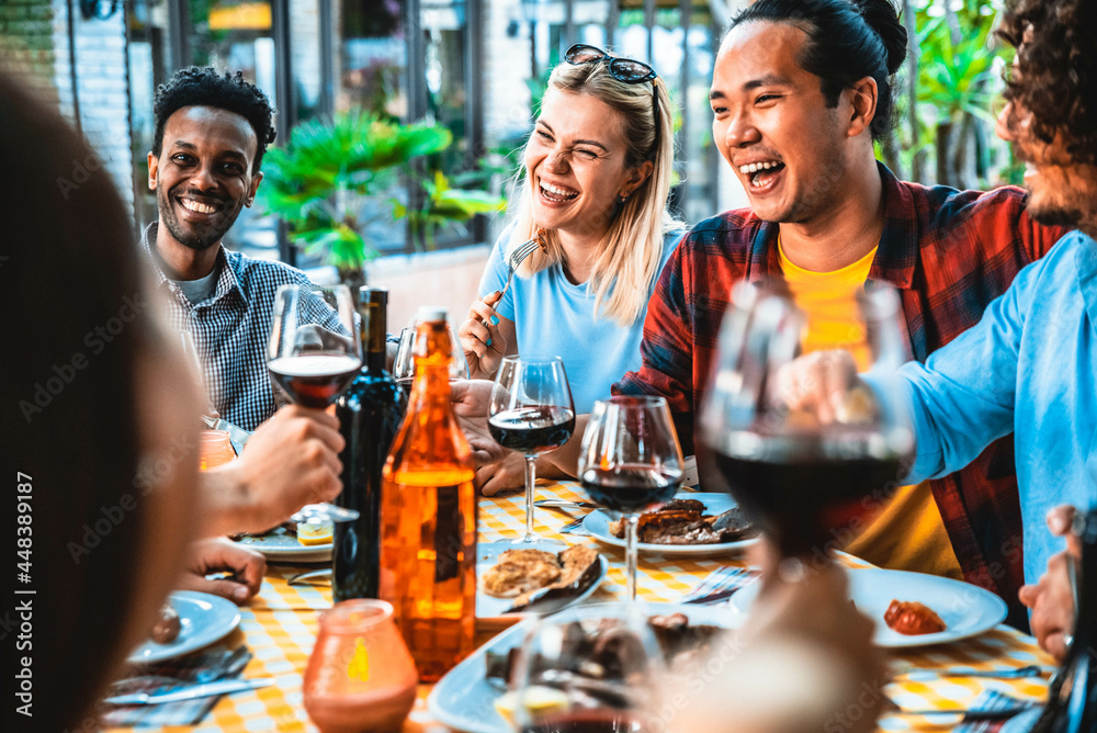 Group of friends having fun at bbq dinner outdoor in garden restaurant - Multiracial people eating food at barbecue backyard home party - Friendship, youth and party concept	