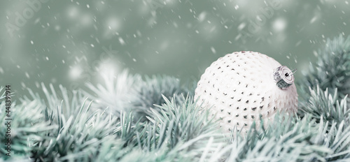 Christmas tree branch with white textured glass bauble and falling snow. Merry Christmas and Happy New Year wide banner