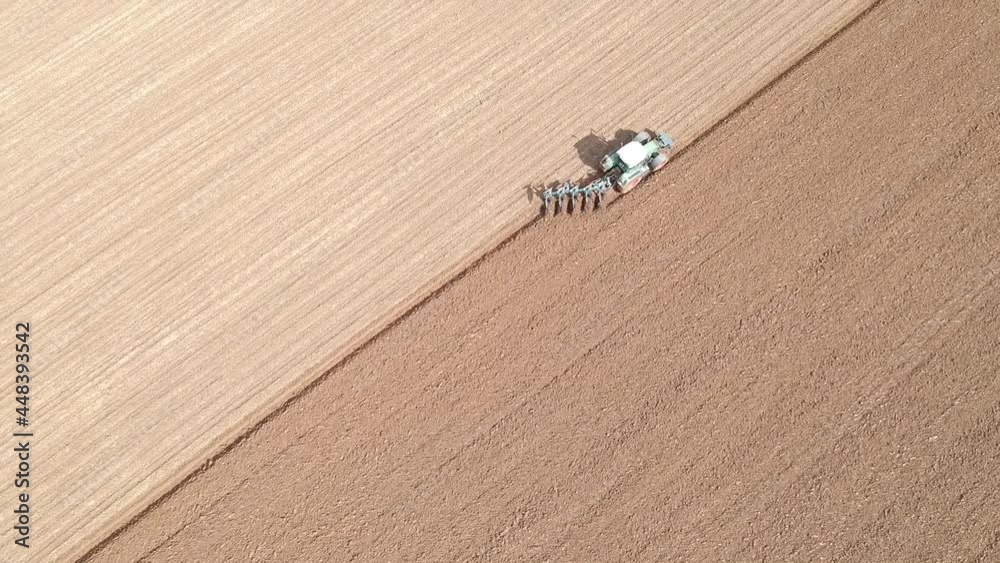 Farming tractor ploughing field diagonally in summer with bright sun following with drone Farming tractor ploughing field diagonally in summer with bright sun following with drone