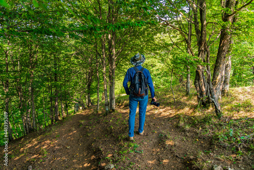 Photographer traveler with a backpack walks in forest along the path