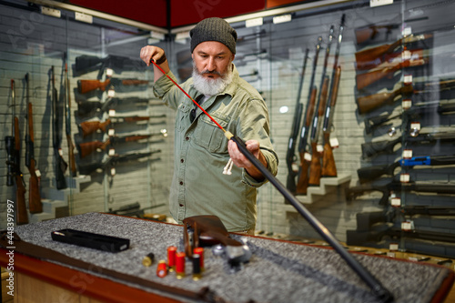 Bearded male hunter choosing ramrod in gun store