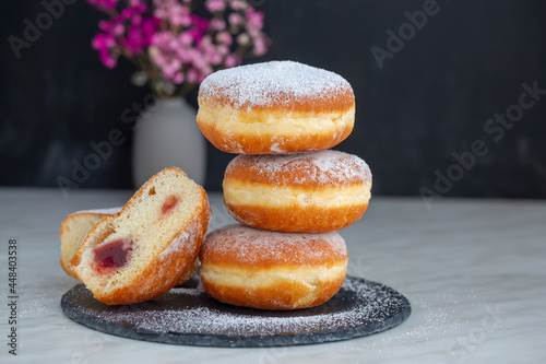 Freshly baked and garnished with powdered sugar German donuts - Berliner or Krapfen - on a white table. Black background. 