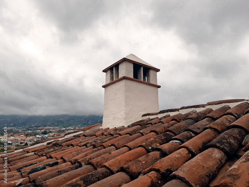 Rustic outdoor fireplace and roof under cloudy gray skies. White work roof chimney. Old tiles on roof with chimney pipe. Red tile roof and chimney horizontally towards the sky. Construction detail