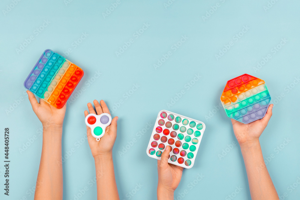 Many hands holding pop it fidget toys on blue background. Push pop-it fidgeting game helps relieve stress, anxiety, autism, provide sensory and tactile experience for children - obrazy, fototapety, plakaty 