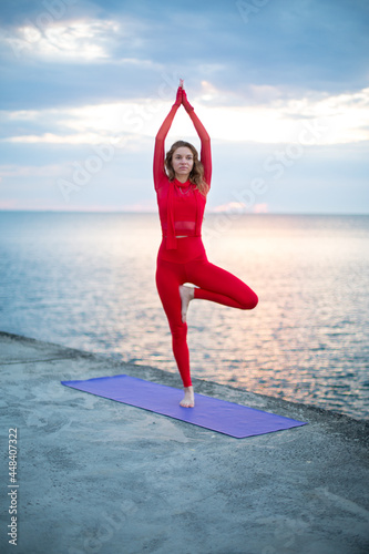 one-legged yoga asana, on the embankment near the sea at dawn with clouds in the sky