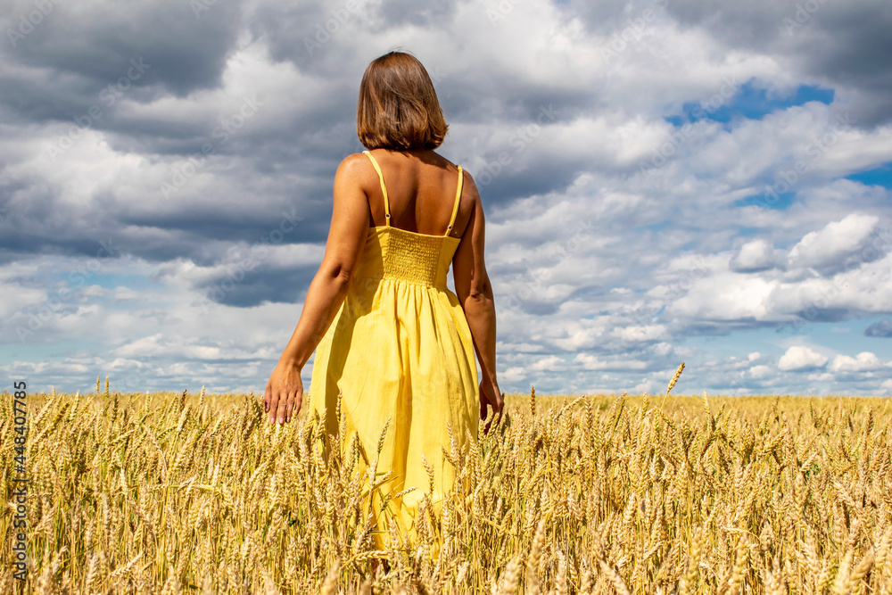Obraz premium A young girl walks across a field of gold and touches the wheat with her palm.