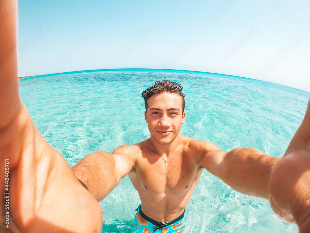 Portrait of happy young man taking a selfie of him in the beach in a blue turquoise water having fun and enjoying alone vacations outdoors.. Portrait of happy young man taking a selfie of him in the beach in a blue turquoise water having fun and enjoying alone vacations outdoors..