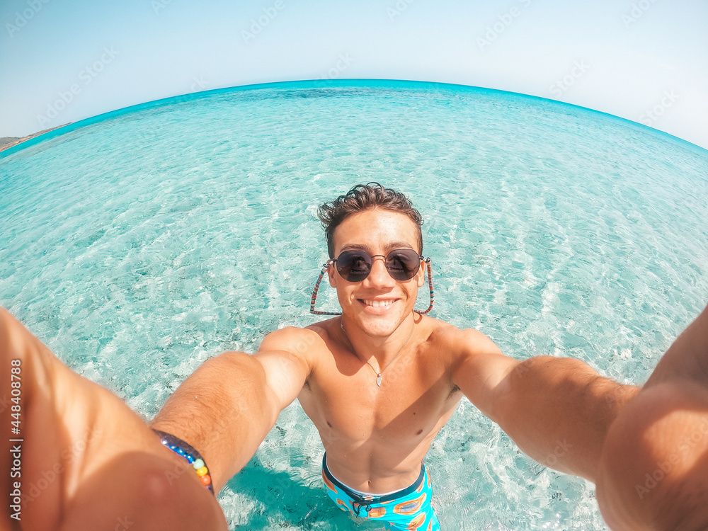 Portrait of happy young man taking a selfie of him in the beach in a blue turquoise water having fun and enjoying alone vacations outdoors..
