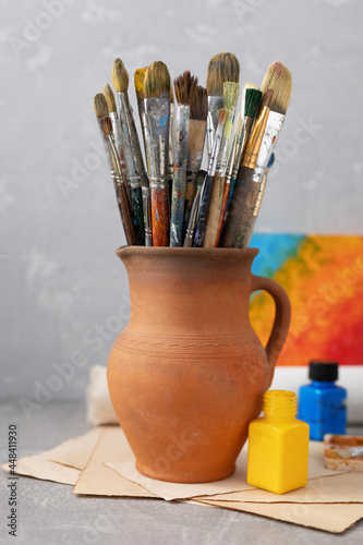Paint brush in clay jug and art painter tool on table background texture. Paintbrush for painting