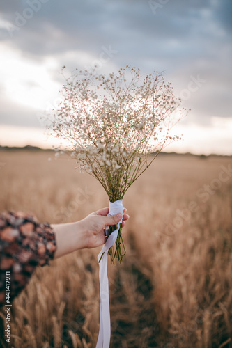 a girl in a sundress, in a field holding a hat and flowers in her hands