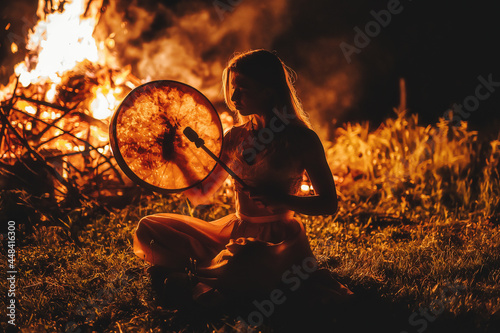 beautiful shamanic girl playing on shaman frame drum in the nature.