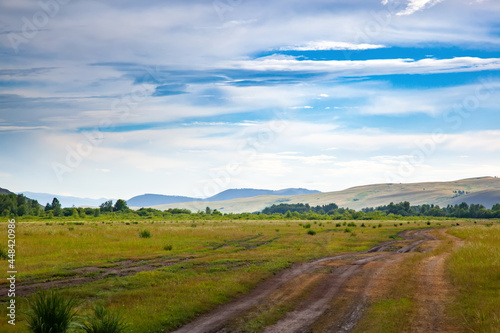 Dirt road in the Khakass steppe.   ountry road in the field. Picturesque clouds over the hills of Khakassia  Russia.