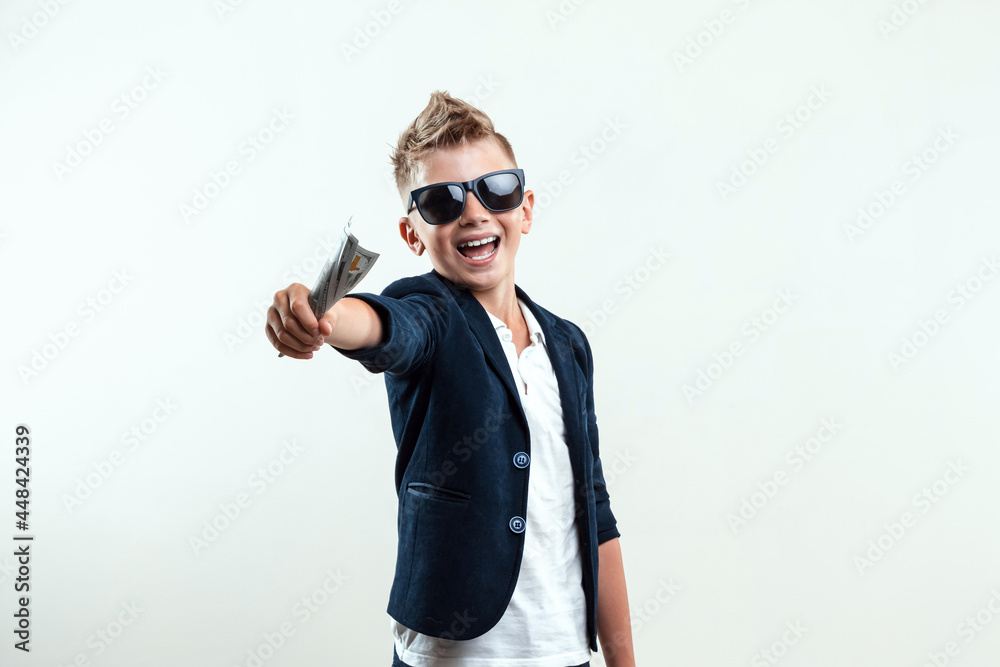 A rich boy on a light background holds a bundle of dollars in his hands. Financial education, young millionaire, investments, loans, winnings, dividends. Copy space. A rich boy on a light background holds a bundle of dollars in his hands. Financial education, young millionaire, investments, loans, winnings, dividends. Copy space.