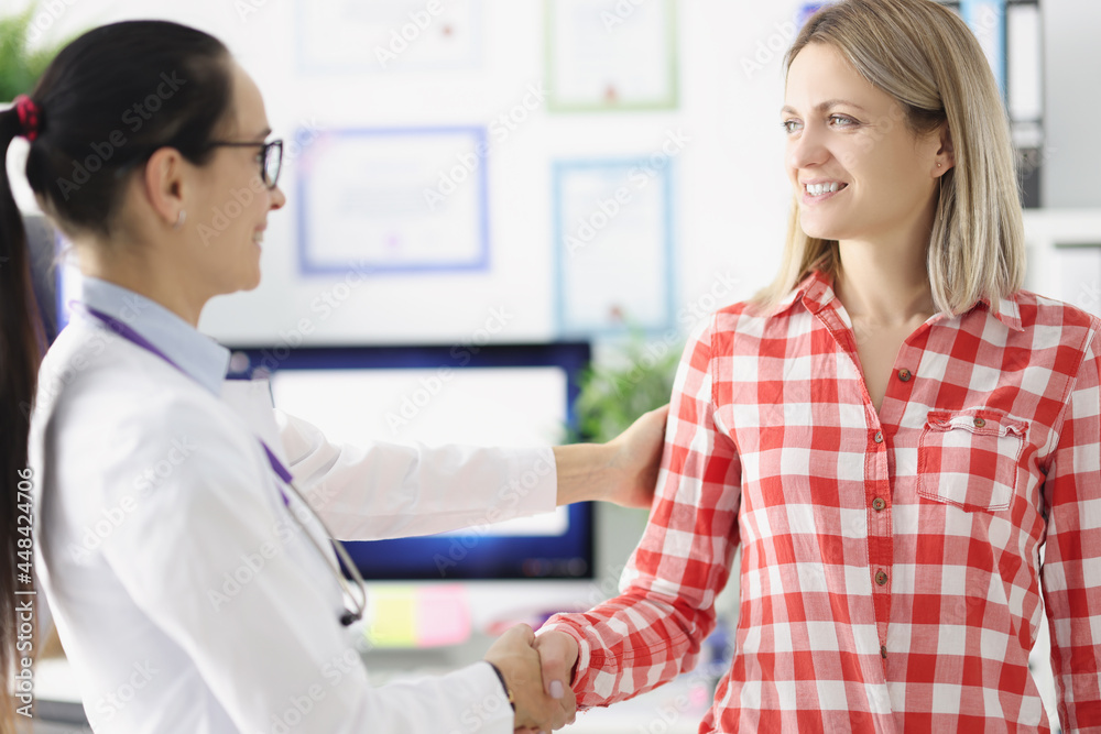 Young smiling female doctor shaking hand to woman patient Young smiling female doctor shaking hand to woman patient