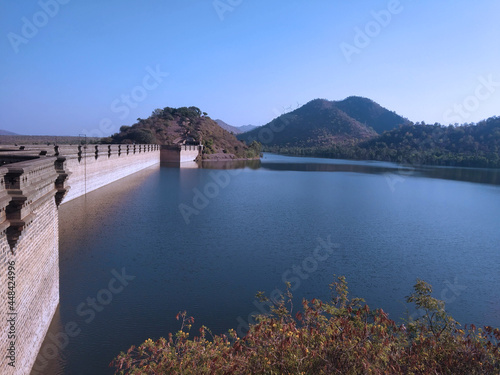 Lake water dam with a cloudy blue sky surrounded by mountains.