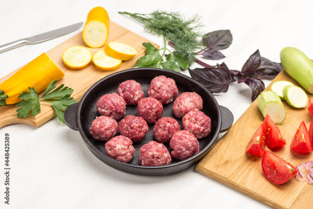 Raw meat balls in frying pan. Sliced tomatoes and zucchini on cutting board. Raw meat balls in frying pan. Sliced tomatoes and zucchini on cutting board.