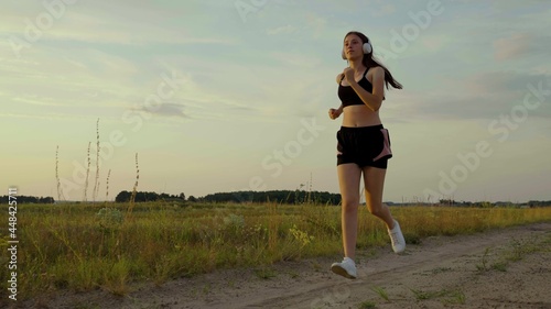 Healthy jogging and outdoor exercise concept. Free young woman runs in summer in park at dawn listens to music with headphones. Training jogging. Listen to music without the Internet and play sports