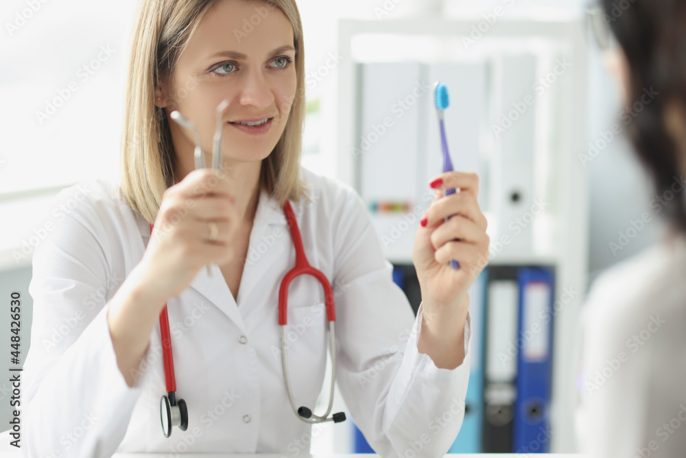 Woman doctor dentist shows patient toothbrush and dental instrument Woman doctor dentist shows patient toothbrush and dental instrument