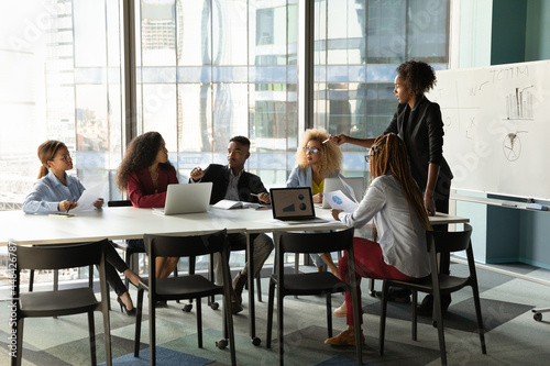 Skilled young female african american business trainer giving professional consultation to motivated group business people, sharing knowledge or developing corporate growth strategy in modern office.