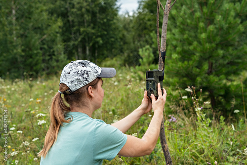 Young woman scientist biologist zoologist sets camera trap for observing wild animals in summer taiga forest to collect scientific data Environmental protection, monitoring of rare and endangered anim photo