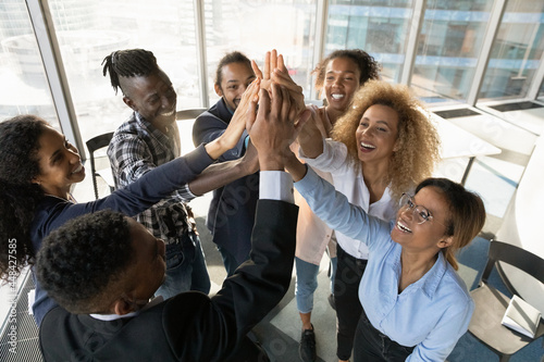 Above top view happy friendly young african american diverse colleagues joining hands in air, celebrating shared corporate success, effective teamwork, raising working spirit, teambuilding concept.